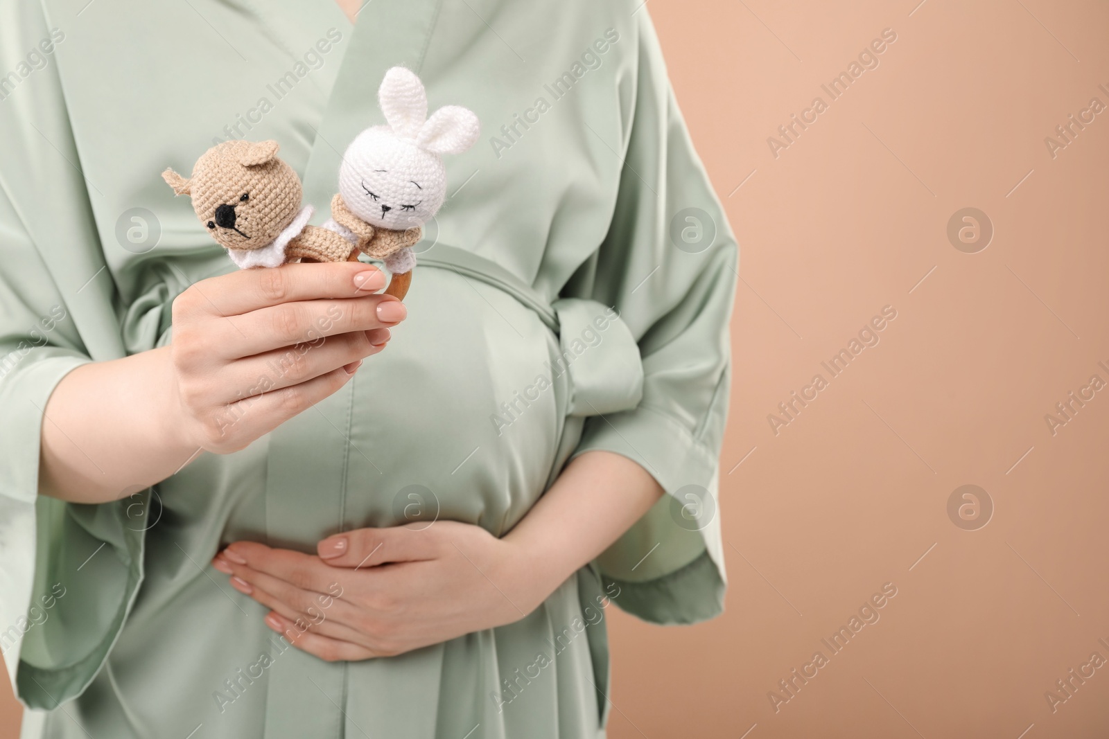 Photo of Expecting twins. Pregnant woman holding two toys on light brown background, closeup. Space for text