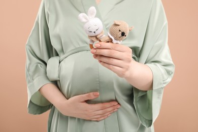 Expecting twins. Pregnant woman holding two toys on light brown background, closeup