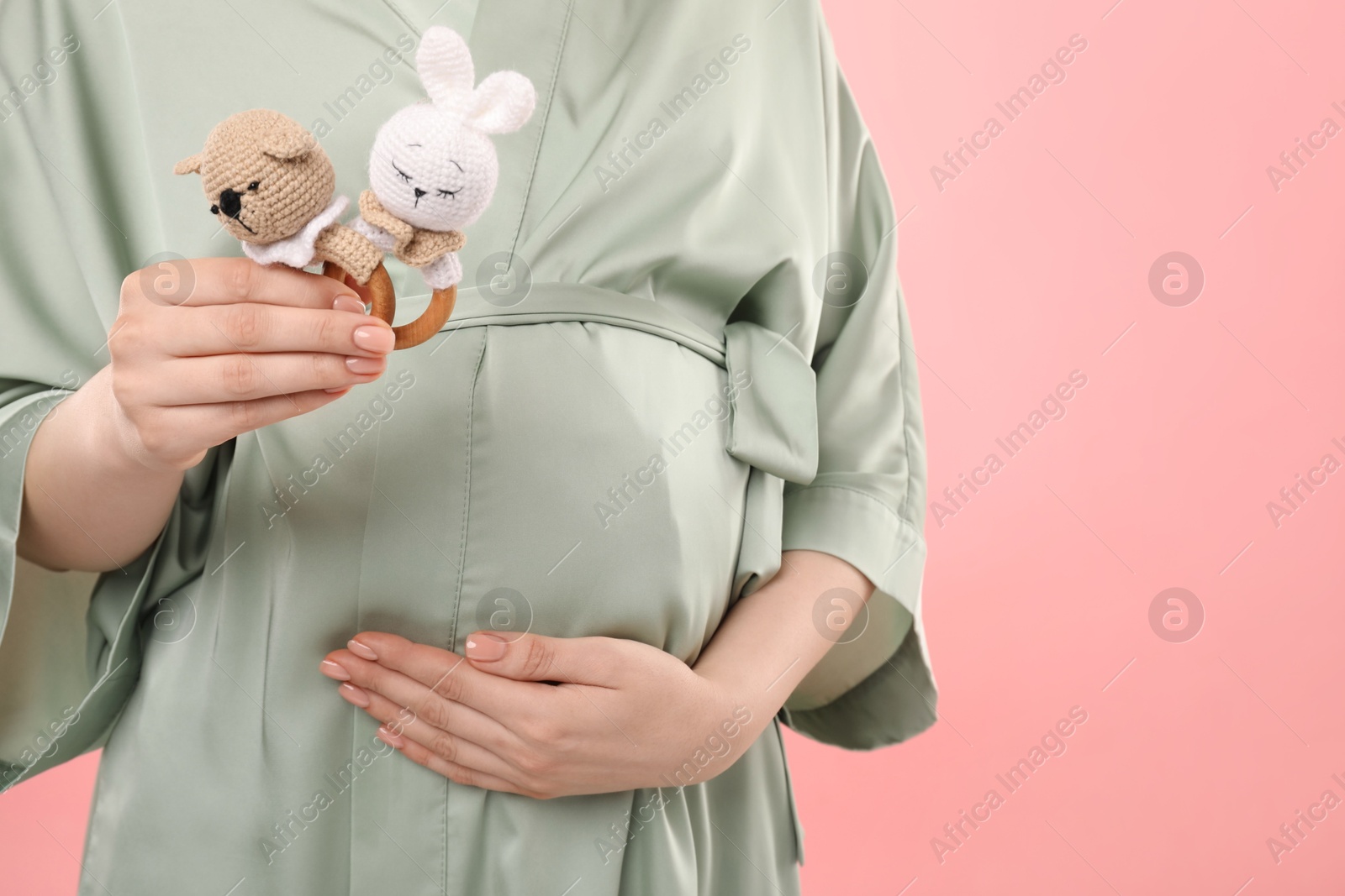 Photo of Expecting twins. Pregnant woman holding two toys on pink background, closeup