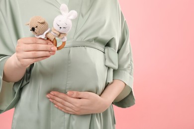 Expecting twins. Pregnant woman holding two toys on pink background, closeup