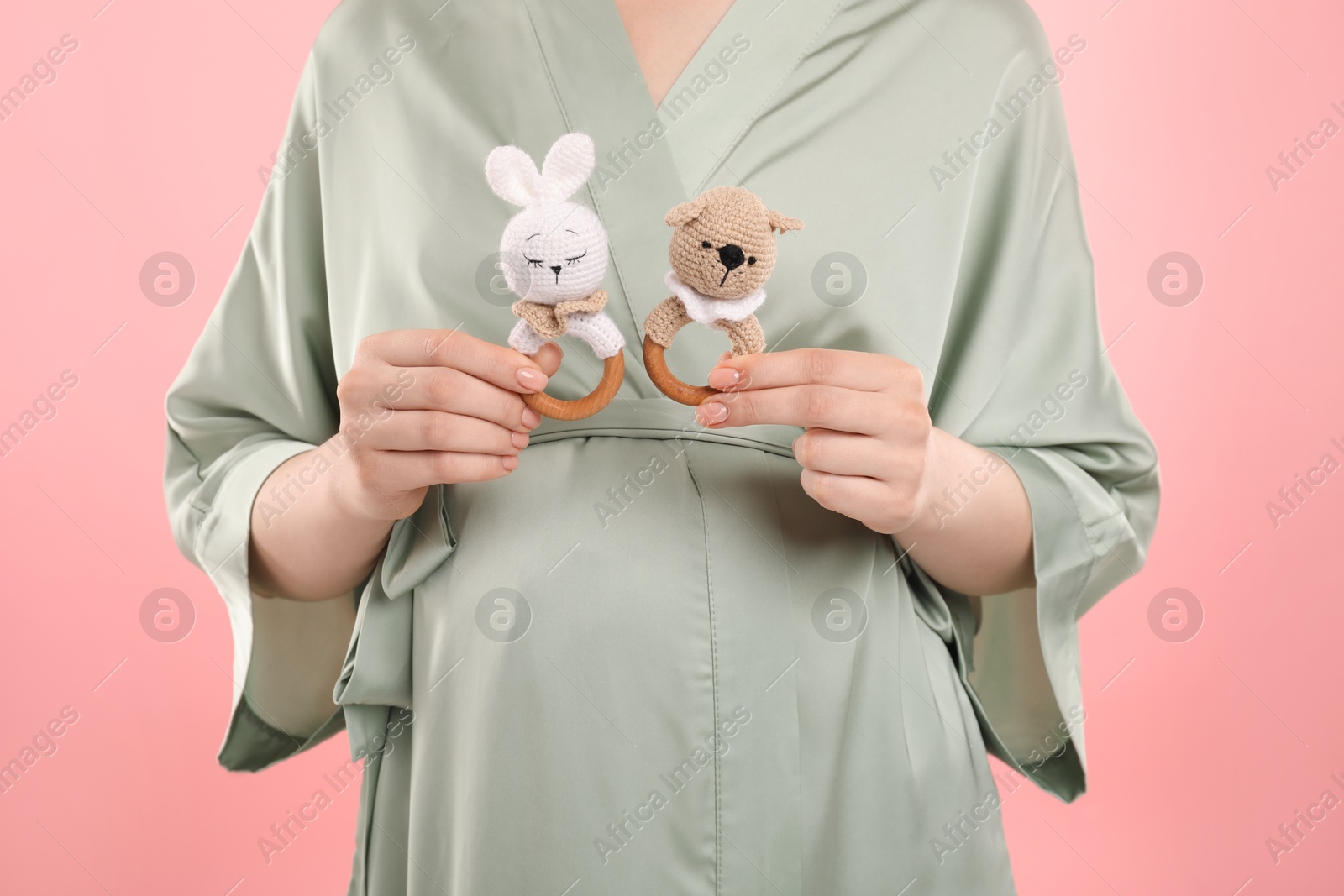 Photo of Expecting twins. Pregnant woman holding two toys on pink background, closeup