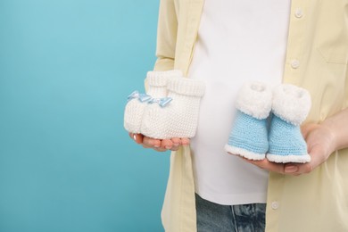 Expecting twins. Pregnant woman holding two pairs of baby shoes on light blue background, closeup. Space for text