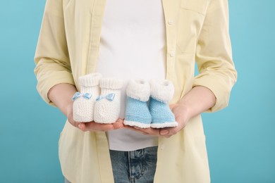 Photo of Expecting twins. Pregnant woman holding two pairs of baby shoes on light blue background, closeup