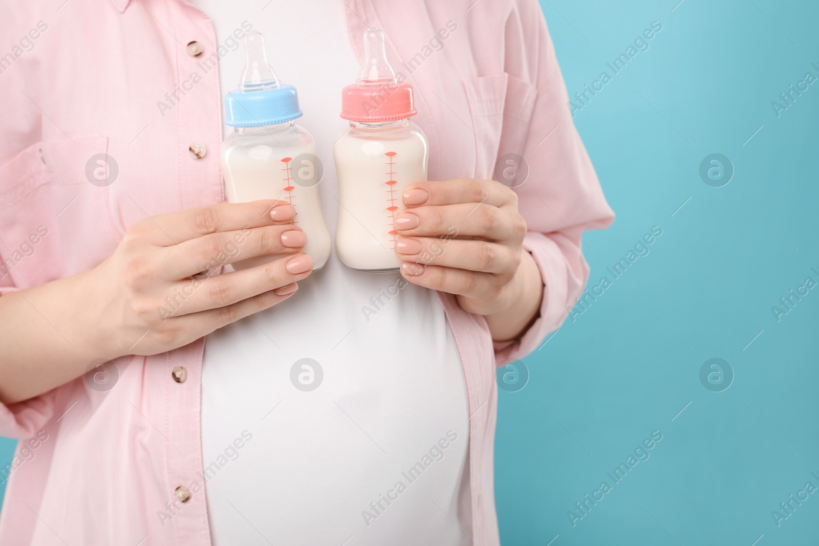 Photo of Expecting twins. Pregnant woman holding two bottles with milk on light blue background, closeup