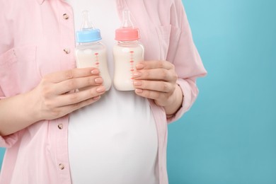 Photo of Expecting twins. Pregnant woman holding two bottles with milk on light blue background, closeup