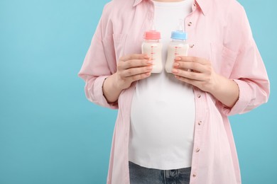 Photo of Expecting twins. Pregnant woman holding two bottles with milk on light blue background, closeup