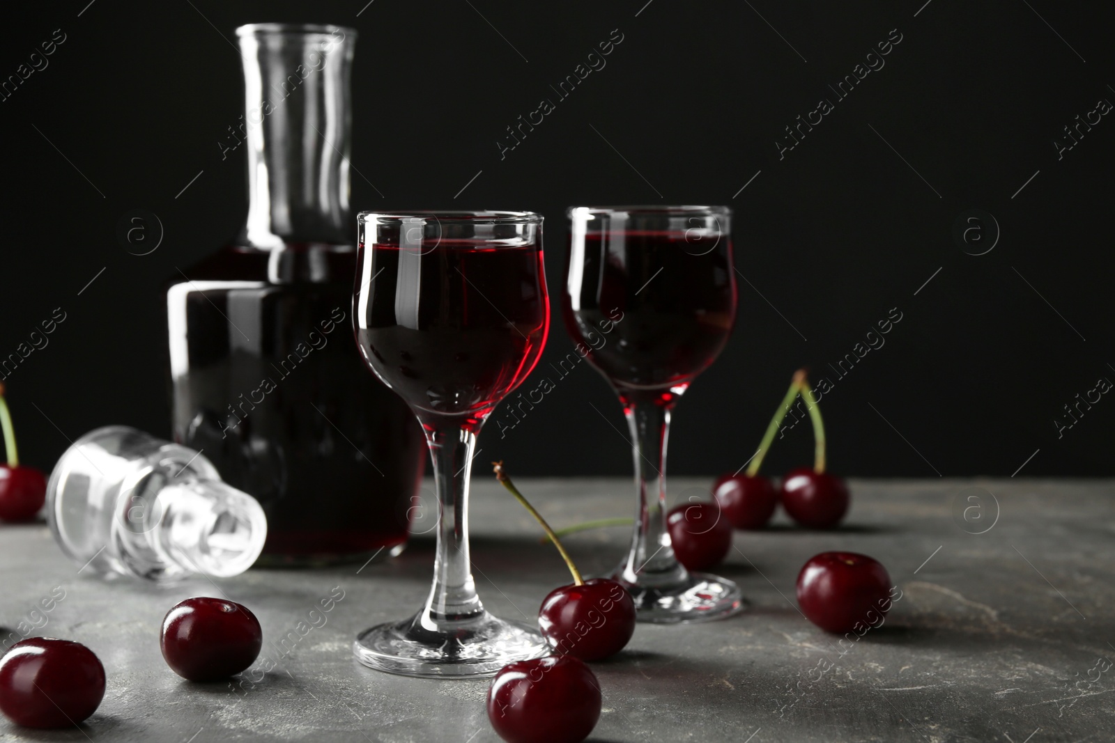 Photo of Delicious cherry liqueur in shot glasses, decanter and fresh berries on grey table