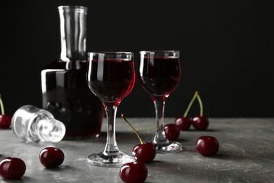 Delicious cherry liqueur in shot glasses, decanter and fresh berries on grey table