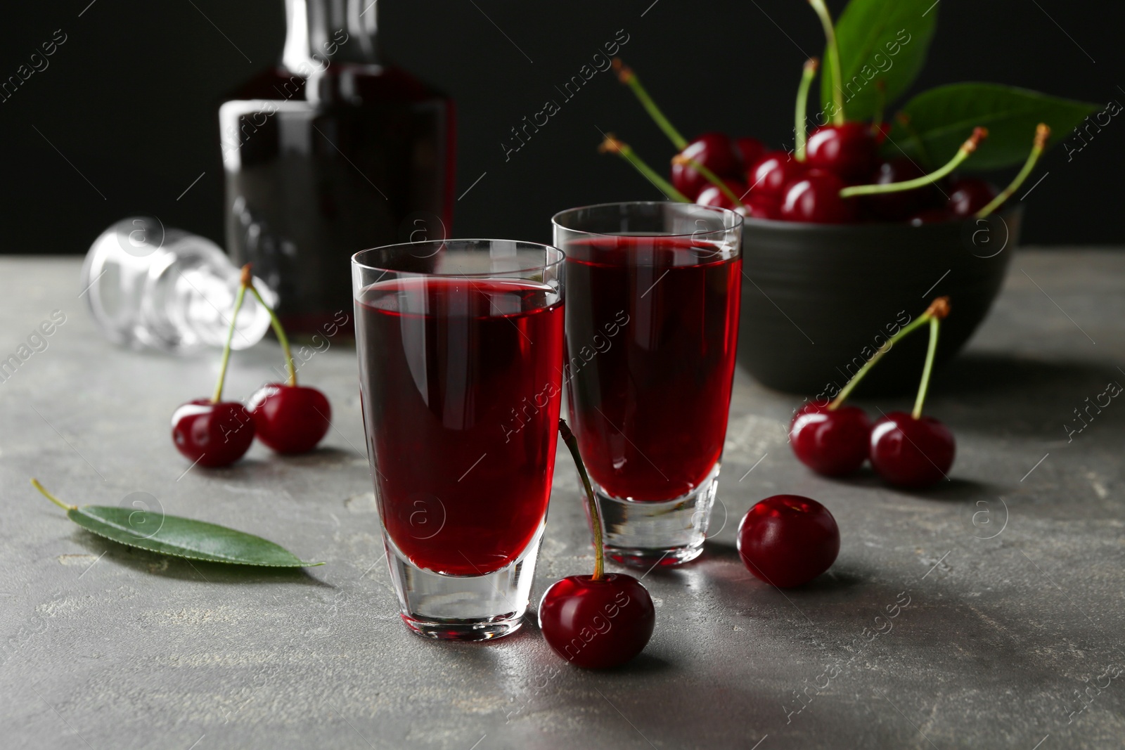 Photo of Delicious cherry liqueur in shot glasses and fresh berries on grey table