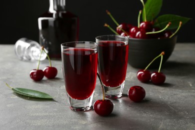 Photo of Delicious cherry liqueur in shot glasses and fresh berries on grey table