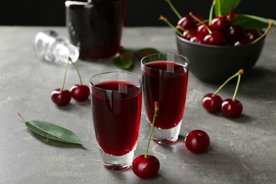 Photo of Delicious cherry liqueur in shot glasses and fresh berries on grey table