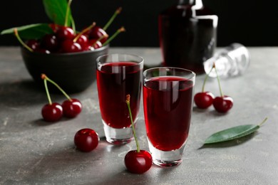 Photo of Delicious cherry liqueur in shot glasses and fresh berries on grey table