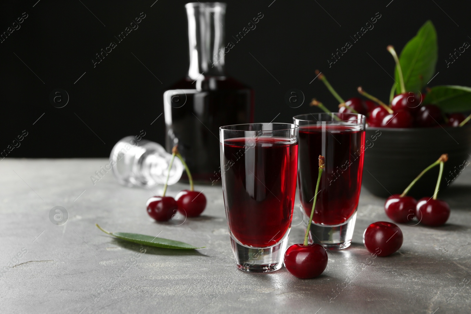 Photo of Delicious cherry liqueur in shot glasses and fresh berries on grey table