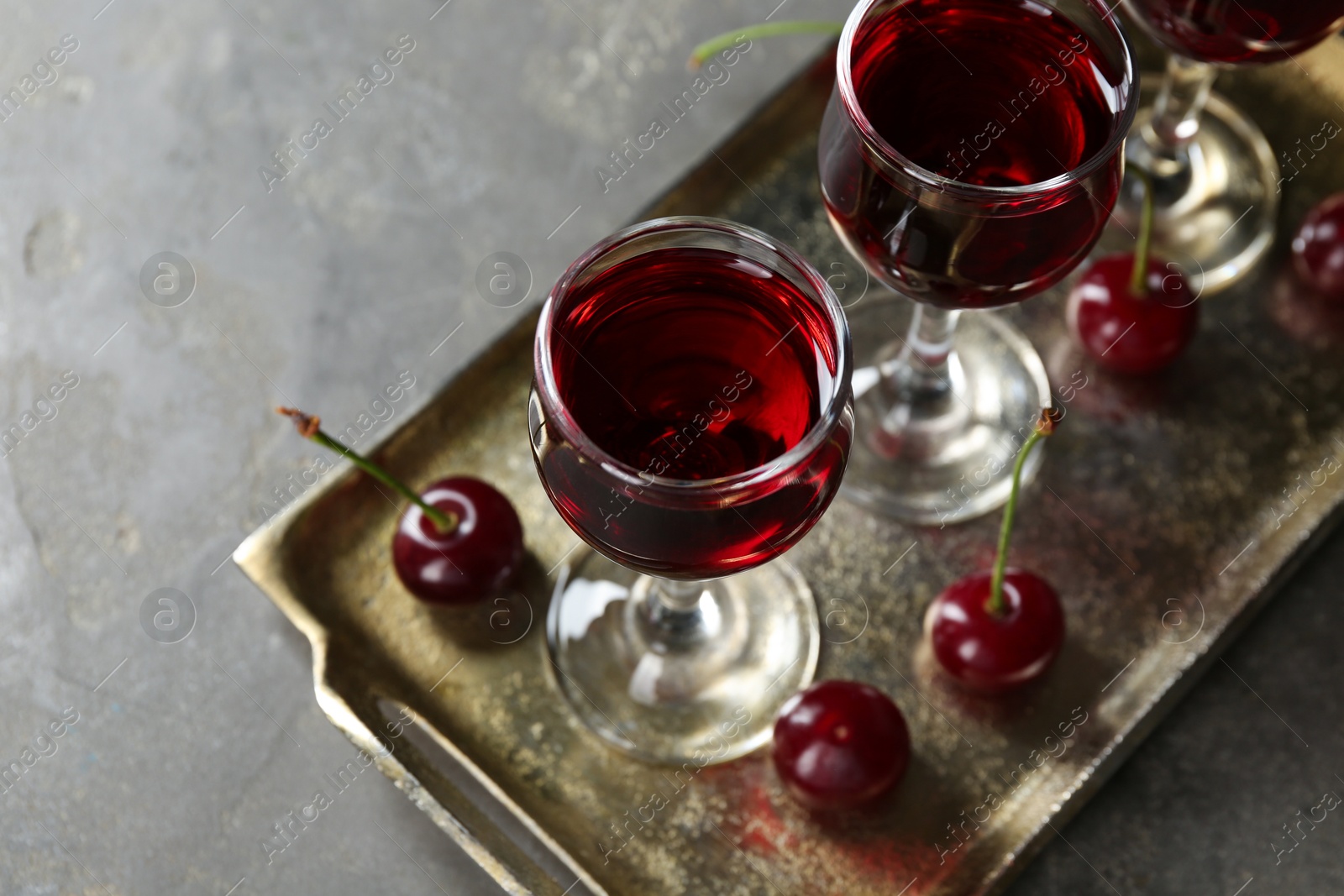 Photo of Delicious cherry liqueur in glasses and fresh berries on grey table