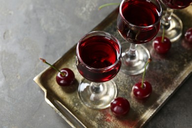 Photo of Delicious cherry liqueur in glasses and fresh berries on grey table