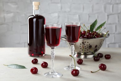 Delicious cherry liqueur in glasses, fresh berries and bottle on light grey table