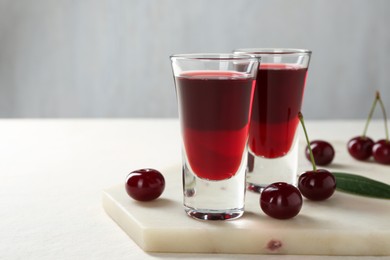 Photo of Delicious cherry liqueur in shot glasses and berries on white table, closeup. Space for text