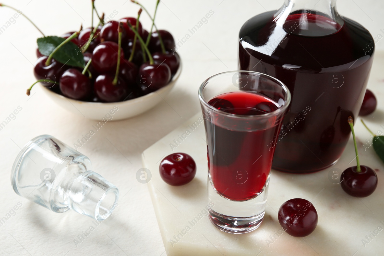 Photo of Delicious cherry liqueur and berries on white table, closeup