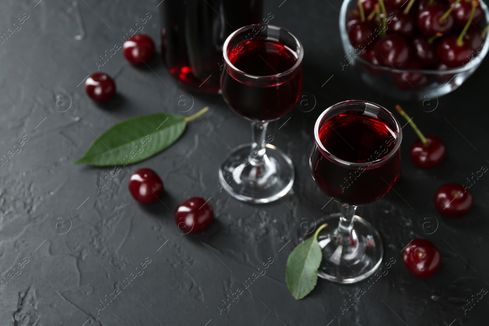 Photo of Delicious cherry liqueur in glasses and berries on black table, closeup