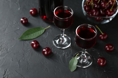 Photo of Delicious cherry liqueur in glasses and berries on black table, closeup