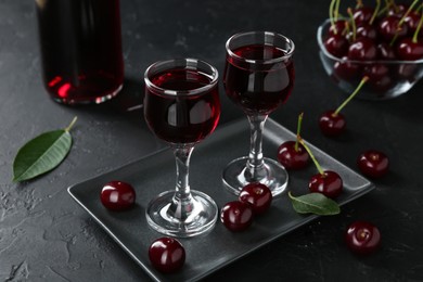 Photo of Delicious cherry liqueur in glasses and berries on black table