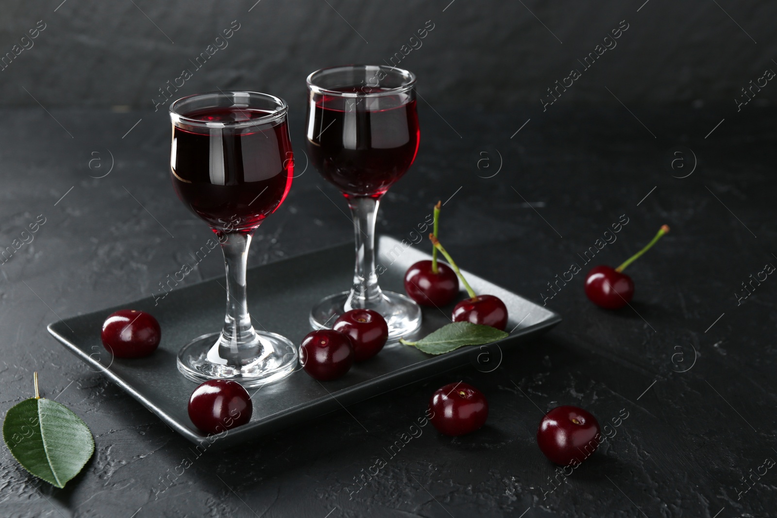 Photo of Delicious cherry liqueur in glasses and berries on black table. Space for text