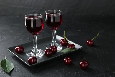 Photo of Delicious cherry liqueur in glasses and berries on black table. Space for text