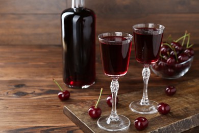 Photo of Delicious cherry liqueur and berries on wooden table