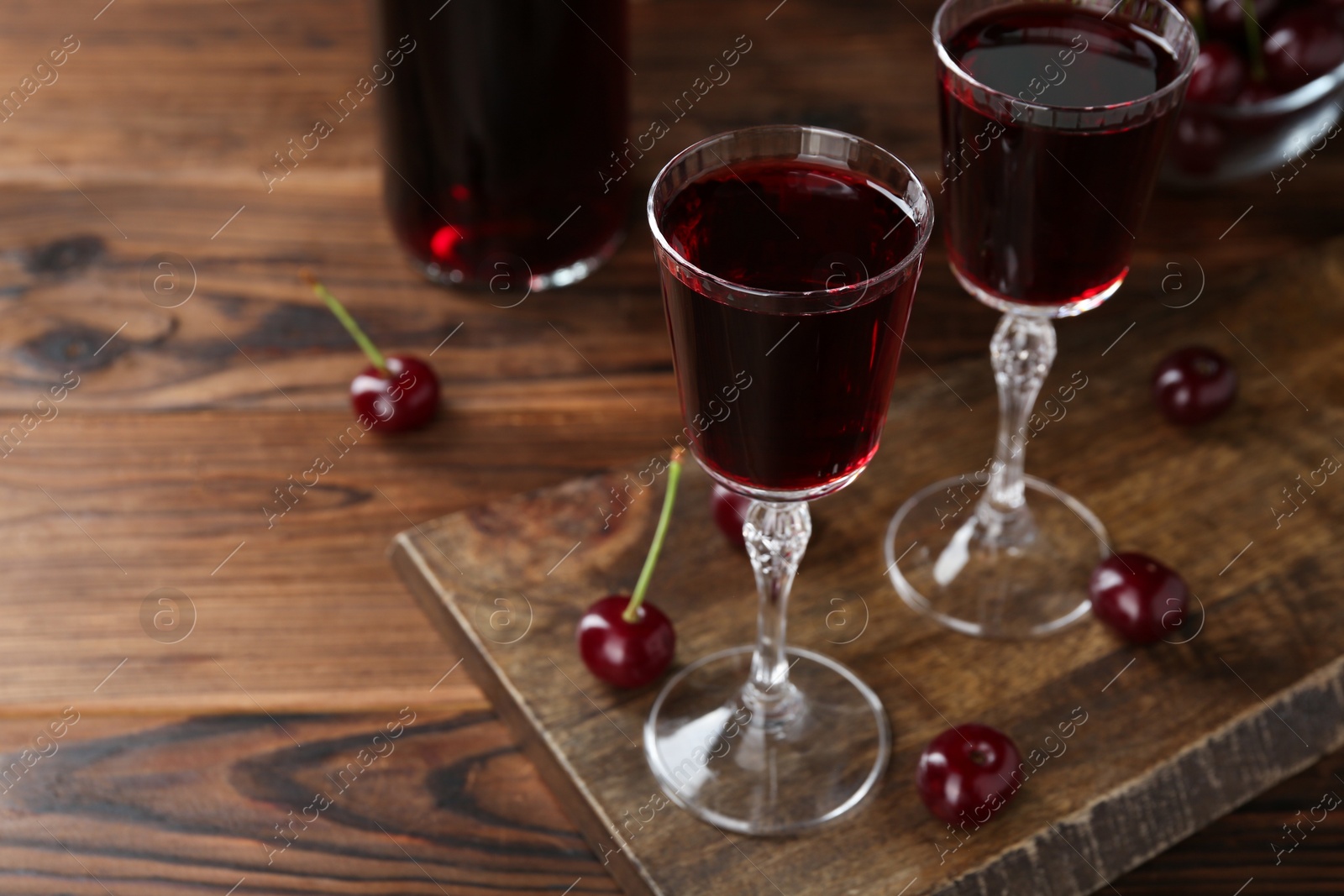 Photo of Delicious cherry liqueur in glasses and berries on wooden table, closeup. Space for text