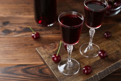 Photo of Delicious cherry liqueur in glasses and berries on wooden table, closeup. Space for text