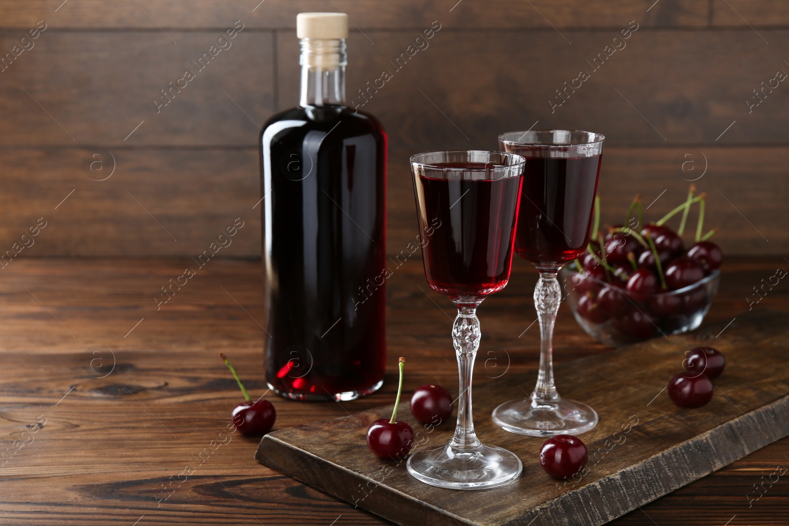 Photo of Delicious cherry liqueur and berries on wooden table