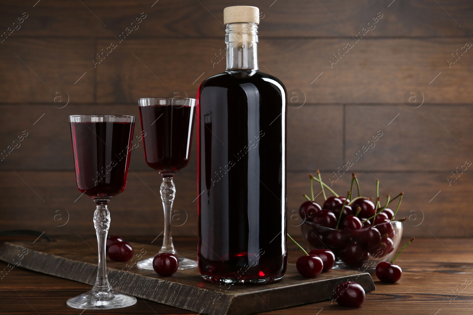 Photo of Delicious cherry liqueur and berries on wooden table