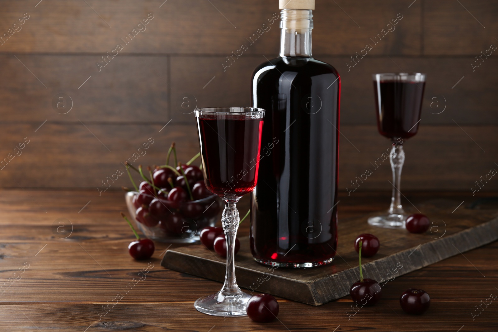 Photo of Delicious cherry liqueur and berries on wooden table