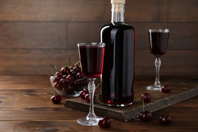 Photo of Delicious cherry liqueur and berries on wooden table