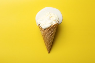 Melted ice cream in wafer cone on yellow background, top view