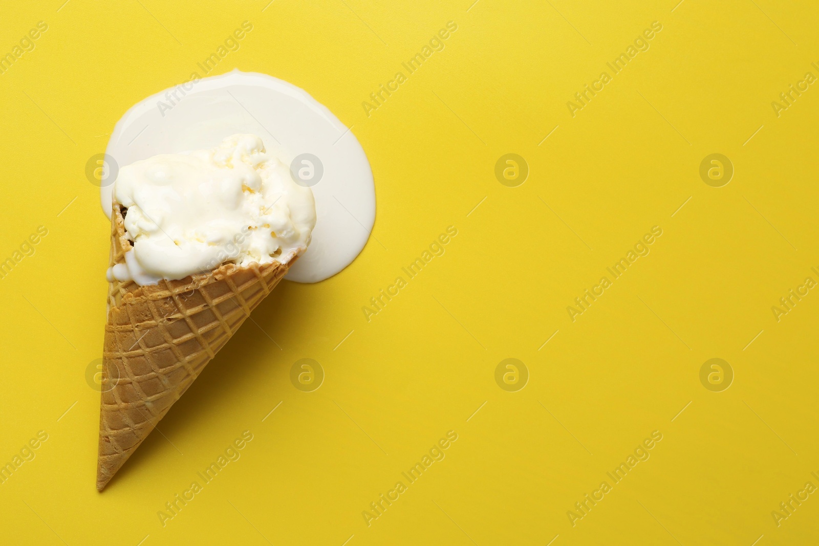 Photo of Melted ice cream in wafer cone on yellow background, top view. Space for text