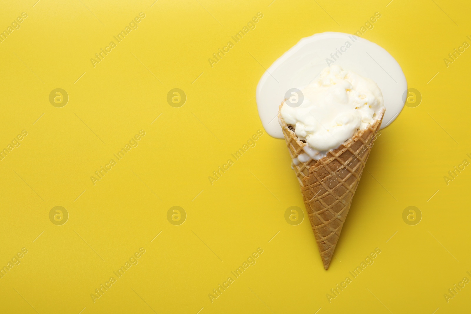 Photo of Melted ice cream in wafer cone on yellow background, top view. Space for text