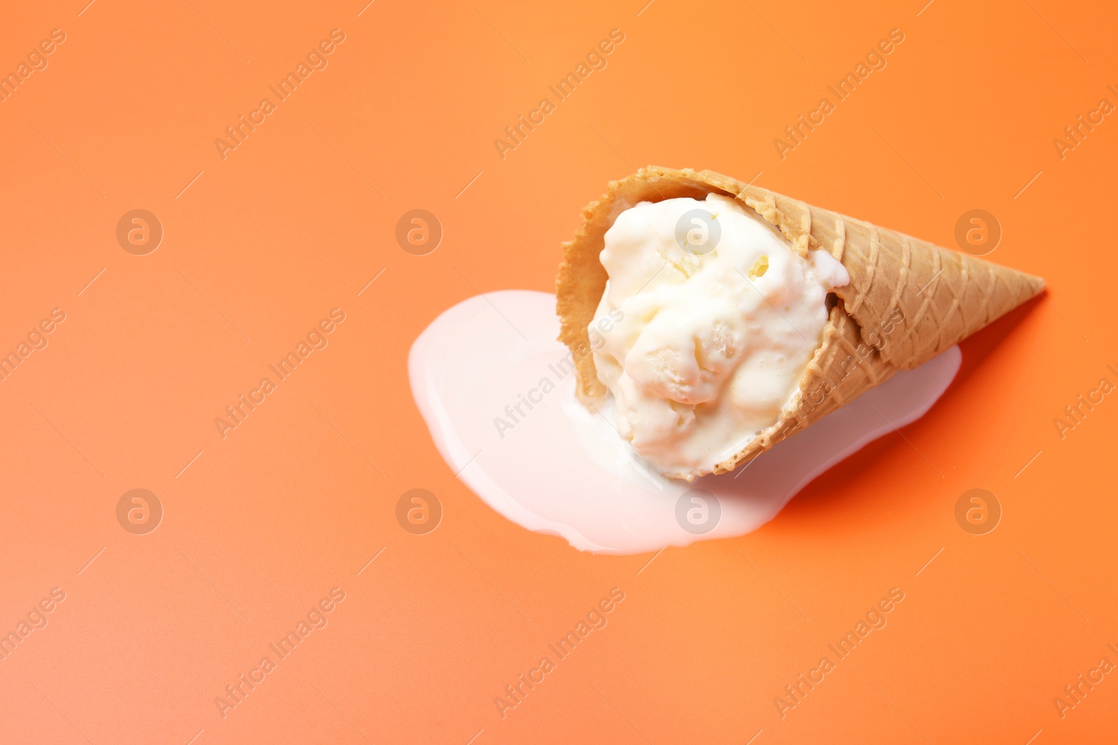 Photo of Melted ice cream in wafer cone on orange background. Space for text