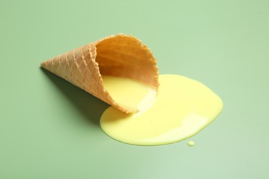 Melted ice cream and wafer cone on light green background