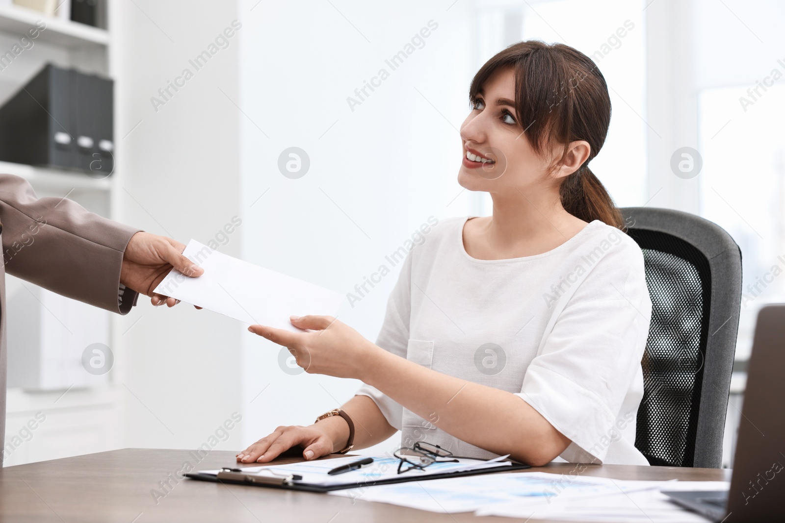 Photo of Smiling employee receiving envelope with salary from boss in office