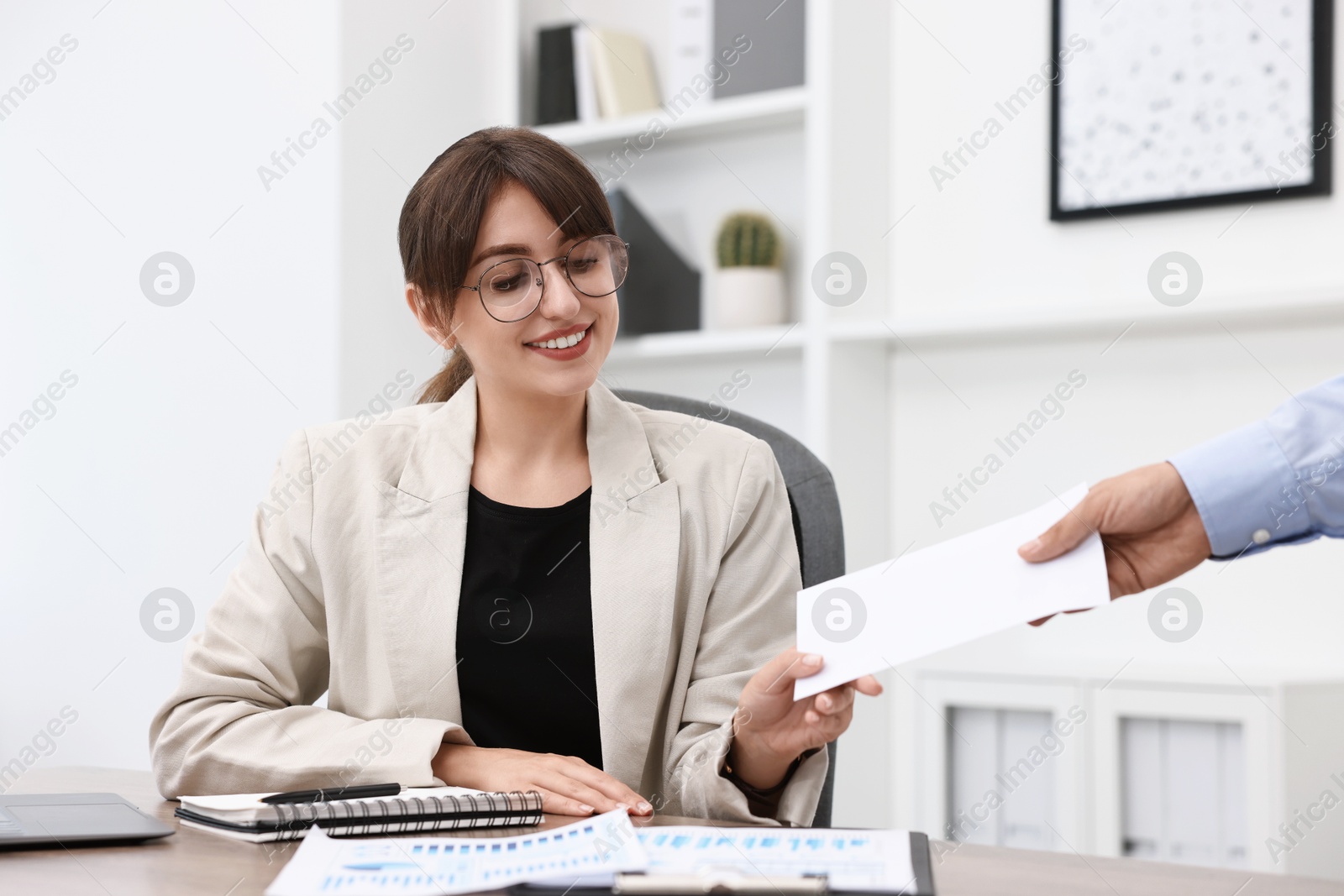 Photo of Smiling employee receiving envelope with salary from boss in office