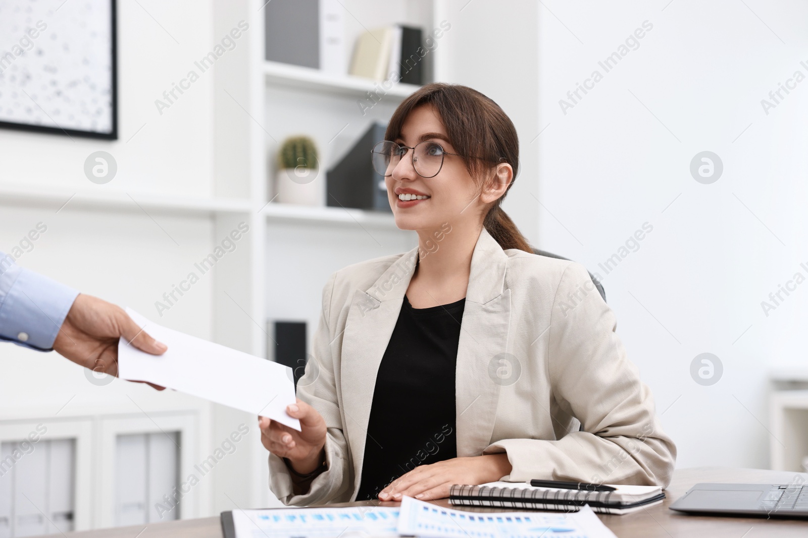 Photo of Smiling employee receiving envelope with salary from boss in office