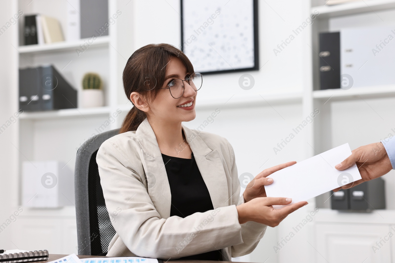 Photo of Smiling employee receiving envelope with salary from boss in office