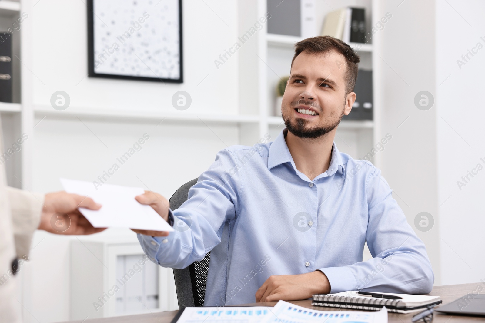 Photo of Smiling employee receiving envelope with salary from boss in office