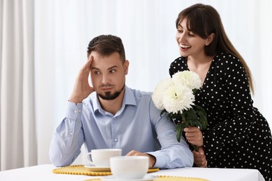 Embarrassed man ignoring smiling woman with flowers indoors