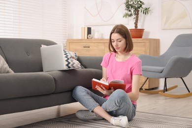 Teenager taking notes while working with laptop at home. Remote job