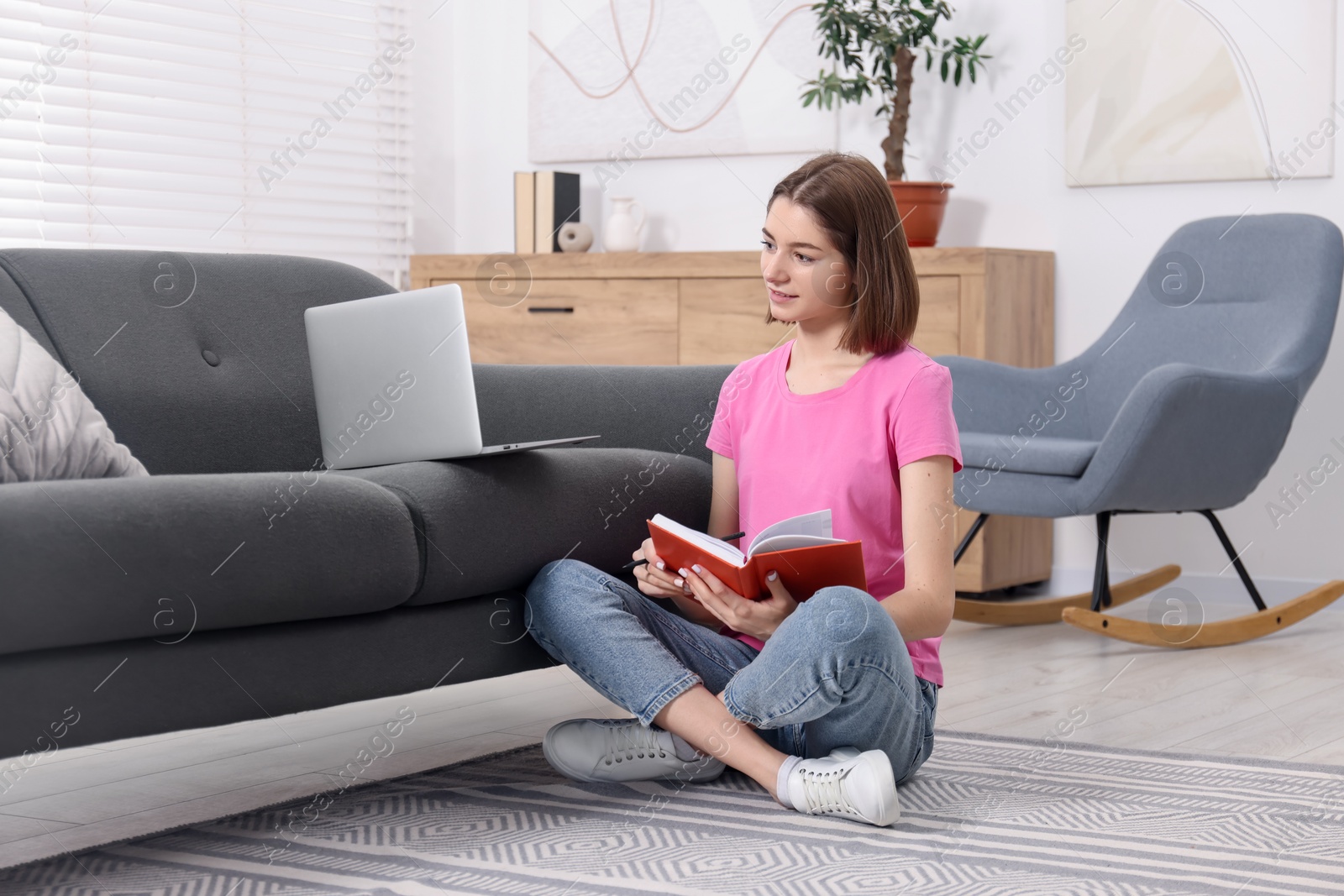 Photo of Teenager taking notes while working with laptop at home. Remote job