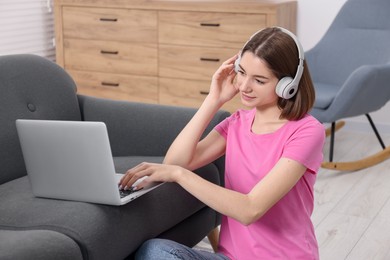 Photo of Teenager in headphones working with laptop at home. Remote job