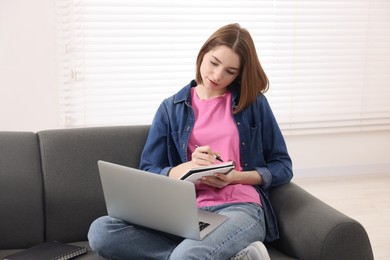 Teenager taking notes while working with laptop at home. Remote job