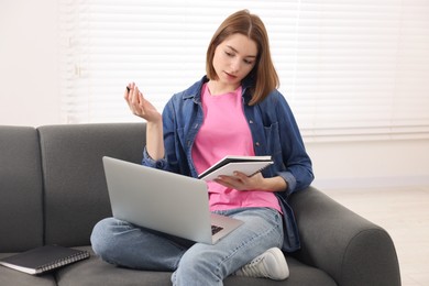 Teenager taking notes while working with laptop at home. Remote job